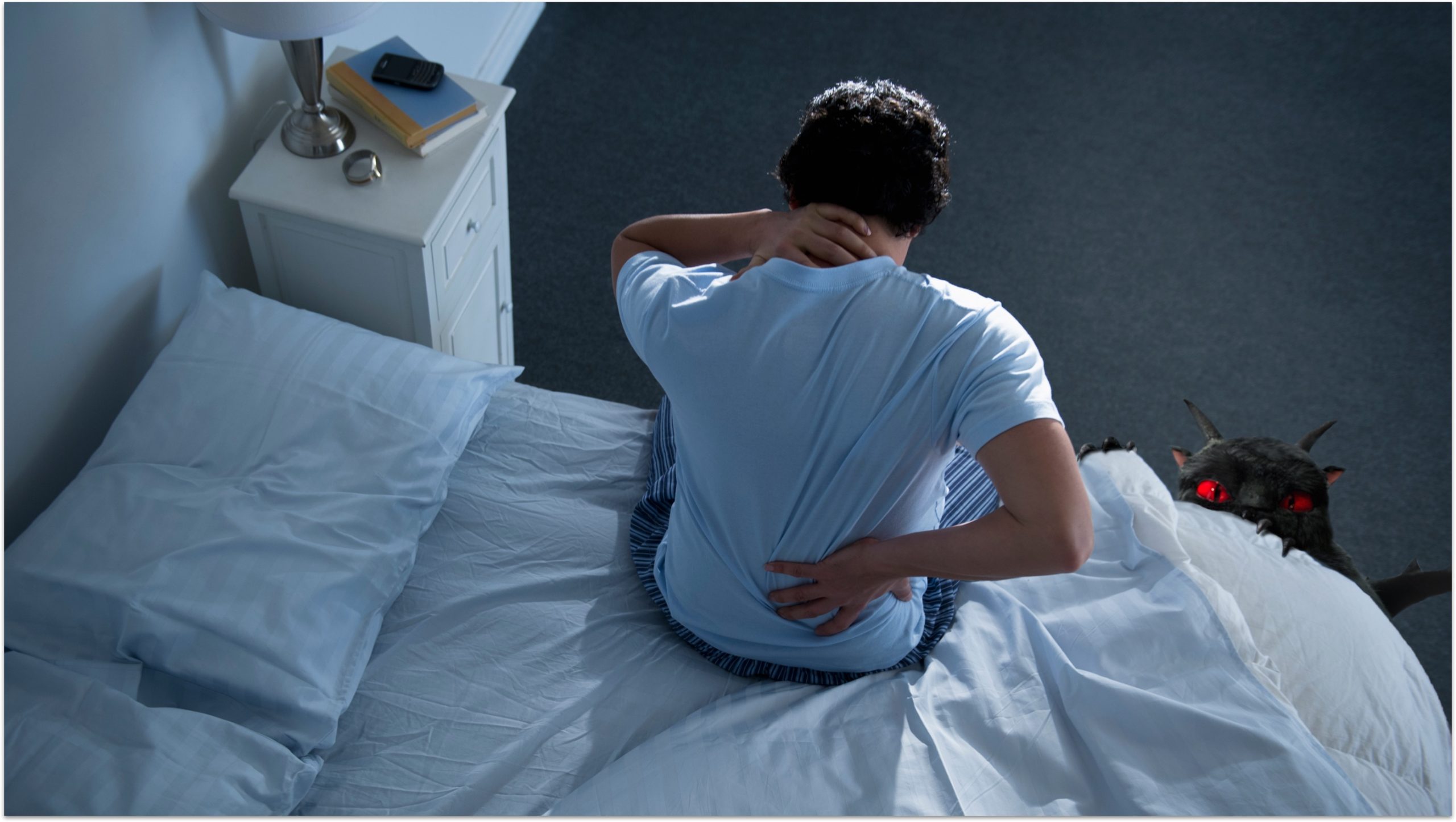 A man sitting on the bed suffering from back pain with monster next to him