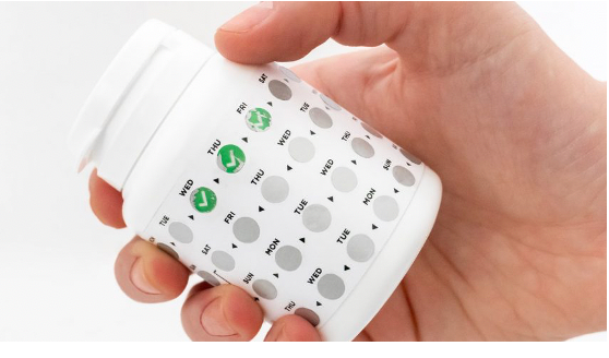Hand holding pill bottle with medication tracker labels
